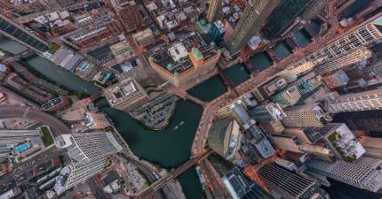 Aerial view of a cityscape with tall buildings, roads, and bridges over intersecting rivers.